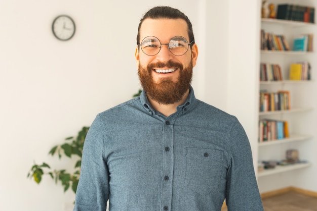 A nice portrait of a young bearded man in a office is smiling 