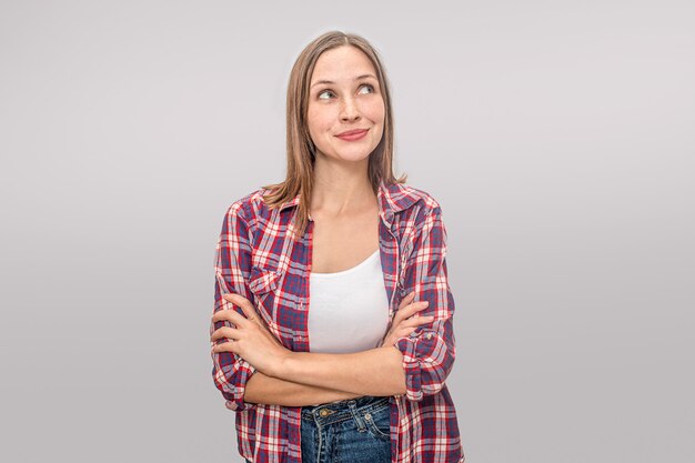 Nice and positive young woman keeps hands crossed and looks up to right.