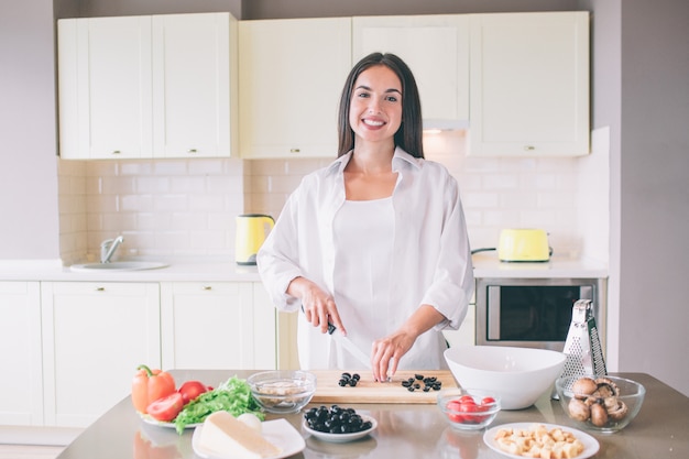 Nice and positive young woman stands and cooks.