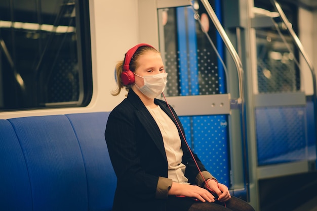 Фото Милая довольно обеспокоенная молодая девушка в маске и наушниках в автобусе, поезде или метро идет в школу