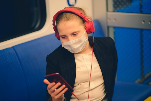 学校に行くバスの電車や地下鉄でマスクとヘッドフォンを身に着けている素敵なかなり心配している若い女の子