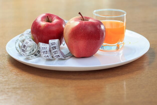 Nice red apples, ruler on plate and multivitamin juice in glass on the table