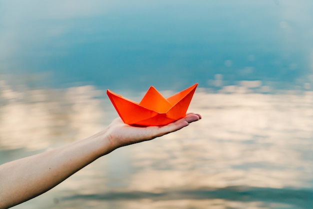 Nice red paper boat on the hand of a young woman above the water in the river 