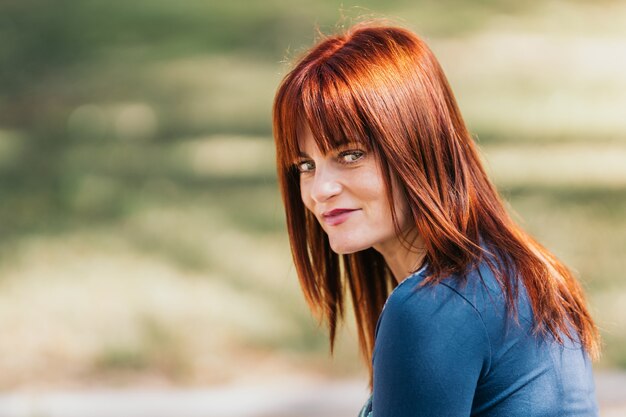 Nice redhead woman looking at the camera in park on a sunny day.