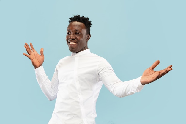 Nice to see you. Young african-american man isolated on blue studio background, facial expression. Beautiful male half-lenght portrait. Concept of human emotions, facial expression. Friendly jesture.