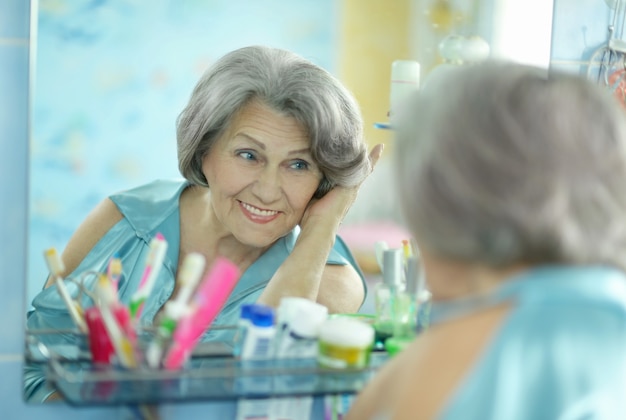 Хорошая старшая женщина делает макияж в ванной