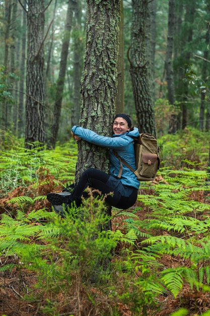 Милая улыбающаяся девушка обнимает ствол дерева посреди леса любовь к природе