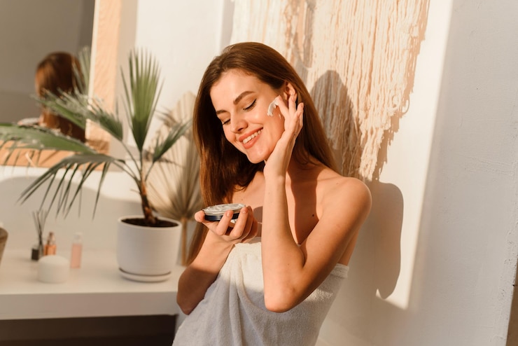 Photo nice smiling lady applying moisturizer to her face in a modern bathroom.