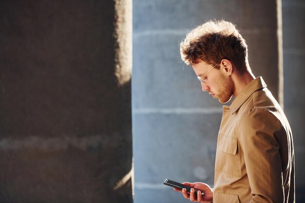 nice sunshine holding phone in hand elegant young man in formal classy clothes outdoors in the city