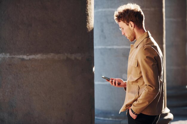 Nice sunshine Holding phone in hand Elegant young man in formal classy clothes outdoors in the city