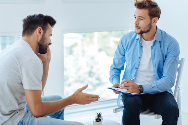 Nice sympathetic handsome doctor listening to his patient and taking notes while doing his job