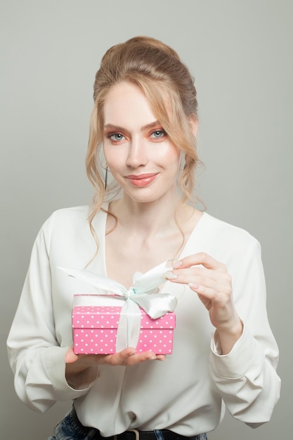 Nice woman holding pink gift on gray background