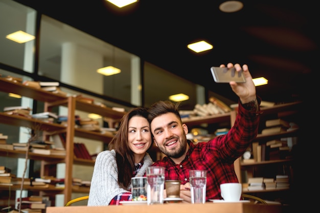 Selfieを取ってモダンなカフェで日付を持っている素敵な若いカップル