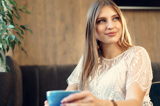 Giovane donna piacevole che gode della tazza di caffè in una caffetteria