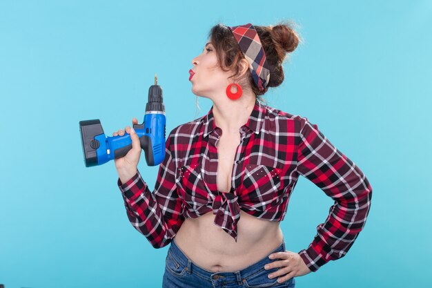 Nice young woman in retro clothes holding a in her hands depicting a pistol on a blue wall