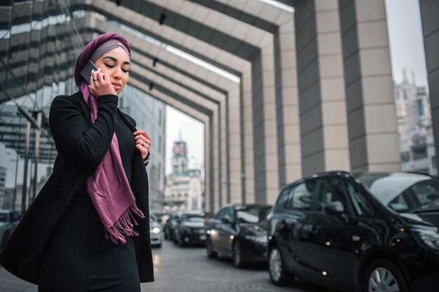 素敵な若い女性が黒い車とポーズの近くに外に立つ