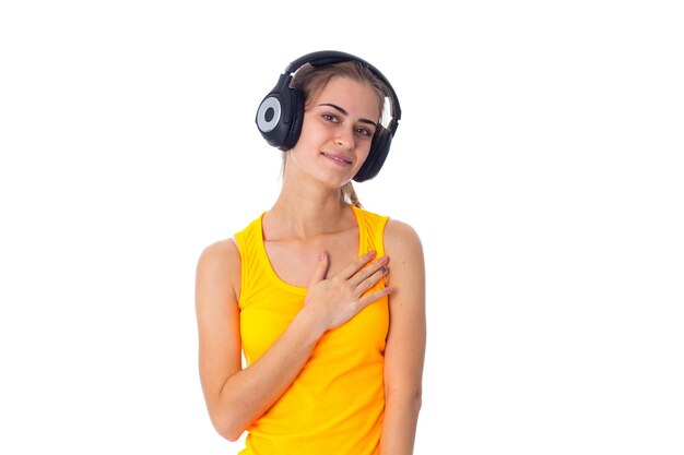 Nice young woman with ponytail in yellow T-shirt and black headphones on white background in studio