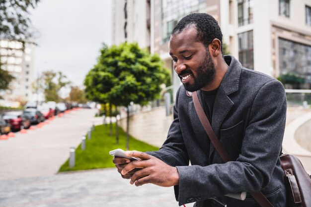 Nicelooking african 30s man using his phone during city walk in\
elegant coat