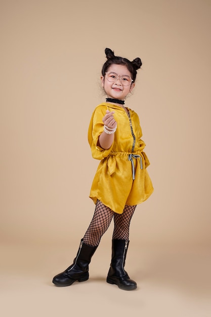 Nicely smiling asian fashion kid girl in yellow dress up on beige background with free text space