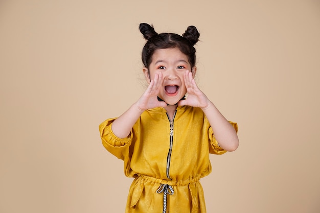 Nicely smiling asian fashion kid girl in yellow dress up on beige background with free text space