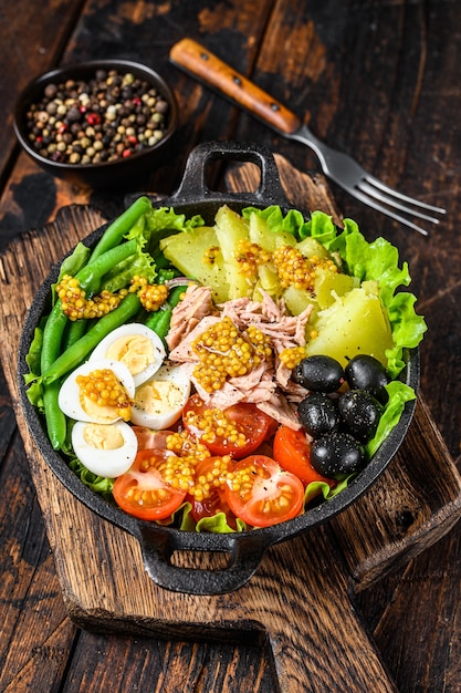 Nicoise salad with tuna,  cherry tomatoes, olives, green beans, cucumber, soft boiled eggs and potato. Dark wooden background. top view.