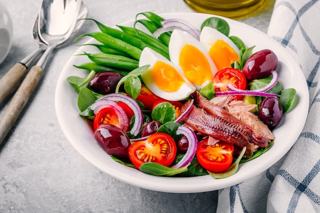 Nicoise salade met tonijn ansjovis eieren sperziebonen olijven tomaten rode uien en salade bladeren op grijze achtergrond