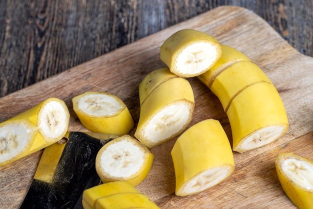 Niet geschilde rijpe gele banaan in stukjes gesneden op een plank