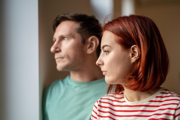 Foto niet glimlachende man en vrouw kijken uit het raam teleurgesteld bewolkt koud weer buiten close-up portret