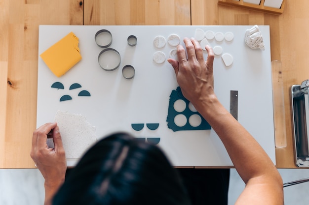 Niet-herkende vrouw die thuis kleurrijke handgemaakte sieraden maakt met klei en gereedschap gebruikt.