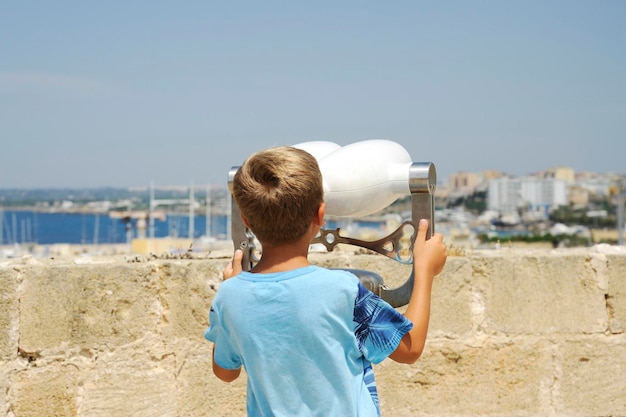 Niet-identificeerbaar blond kind kijkt door de verrekijker naar de zee vanaf het kasteel van Gallipoli, Apulië, Italië