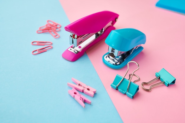 Nietmachine en paperclips close-up, blauwe en roze achtergrond. Kantoorbenodigdheden, accessoires voor school of onderwijs, schrijf- en tekengereedschappen