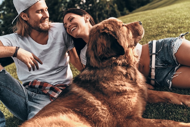 Niets anders dan liefde. Jong modern stel liggend op het gras met hun hond terwijl ze vrije tijd in het park doorbrengen