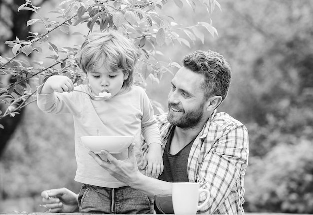 Niets dan familie gezond eten en diëten Zuivelproducten gelukkige vadersdag Kleine jongen met vader eet ontbijtgranen Ochtendontbijt Vegetarisch dieet vader en zoon eten buiten familie dinertijd