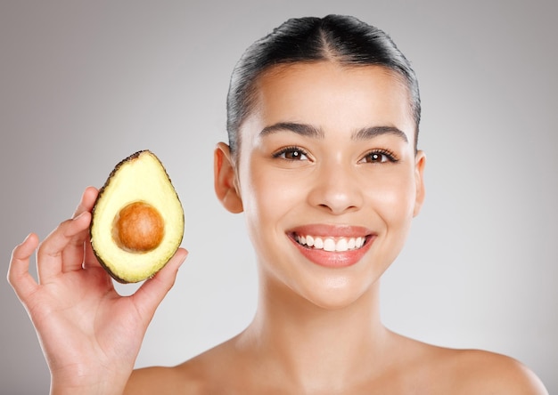 Niets heeft meer natuurlijke oliën dan deze Studio-opname van een aantrekkelijke jonge vrouw die een avocado tegen haar gezicht houdt tegen een grijze achtergrond