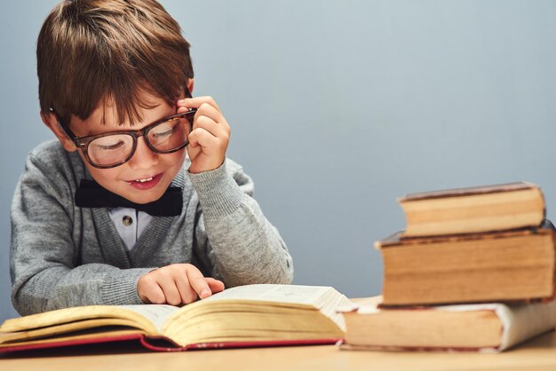 Niets ontwikkelt een geest zoals kennis Studio-opname van een slimme kleine jongen die boeken leest tegen een grijze achtergrond