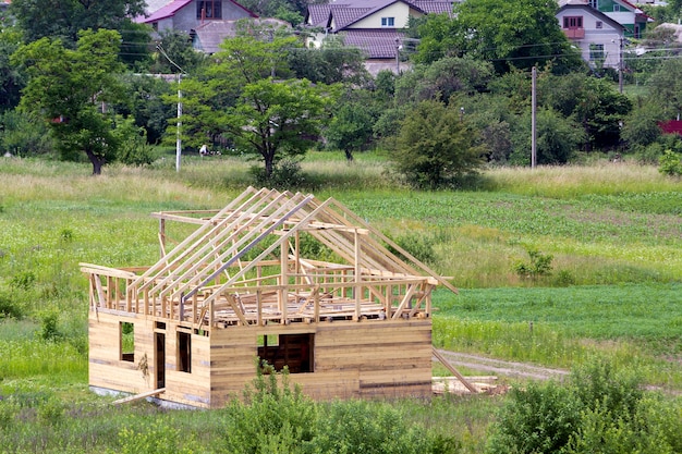 Nieuw houten huisje van natuurlijke houtmaterialen met dakframe van steile planken in aanbouw in groene buurt. Vastgoed, investeringen, professioneel bouwen en wederopbouwconcept.