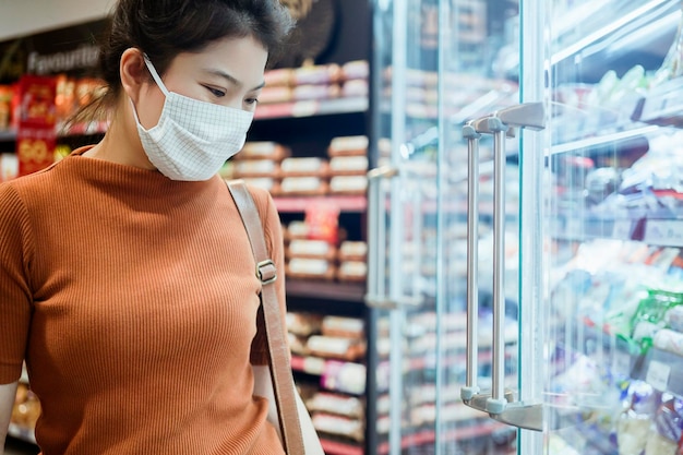 Nieuw normaal na covid-epidemie jonge slimme aziatische vrouw winkelen nieuwe levensstijl in supermarkt met gezichtsschild of maskerbescherming hand kies verse groente van fruit nieuwe normale levensstijl