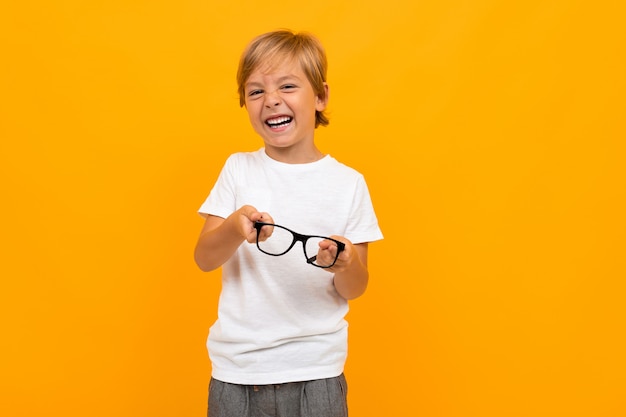 Nieuw visieconcept. jongen in een wit T-shirt loenst met een bril in zijn handen op een gele achtergrond