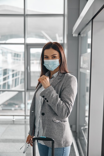 Nieuwe bestelling op luchthavens. Vrouw met masker in terminal met bagage alleen in de buurt van panoramische ramen