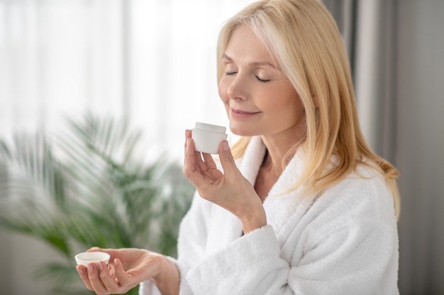 Nieuwe cosmetica. Een blonde vrouw in een witte badjas met een potje nieuwe crème