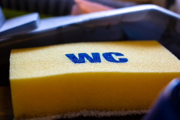 Nieuwe gele spons met het label WC voor het wassen van de toiletpot ligt in de blauwe doos