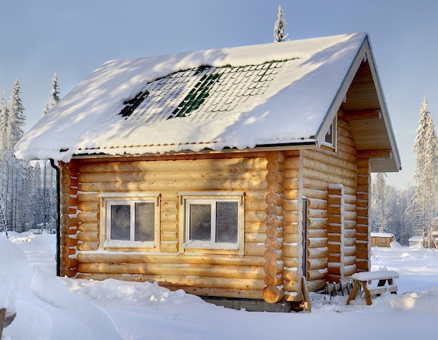 Nieuwe houten Russische sauna op zonnige winterdag, van buitenaf, tegen de achtergrond van besneeuwd bos.