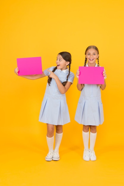 Nieuwe informatie leveren Aankondiging en promotie Schoolmeisjes vrolijke leerlingen die u informeren Schooluniform voor meisjes houdt posters vast Terug naar school Schoolmeisjes houden blanco papier kopieerruimte