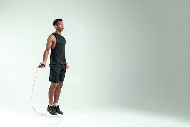 Nieuwe kampioen. Volledige lengte van jonge Afrikaanse man in sportkleding springtouw tijdens het sporten in de studio tegen een grijze achtergrond. Sportuitrusting. Actieve levensstijl