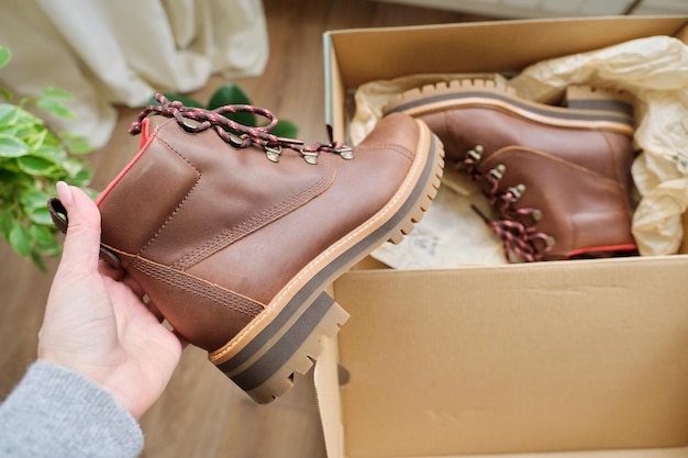 Nieuwe lederen bruine waterdichte wandelschoenen voor de herfst in handen van vrouwelijk, trendy schoeisel voor de winter. Schoenen uitpakken, online winkelen vanuit huis, schoenenwinkel