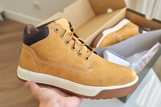 Nieuwe leren bruine waterdichte wandelschoenen in de herfst in handen van vrouwelijk, trendy schoeisel voor de winter. Schoenen uitpakken, online winkelen vanuit huis, schoenenwinkel