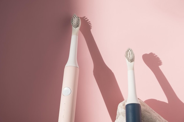 Nieuwe moderne ultrasone tandenborstel. Tandverzorgingsbenodigdheden met witte stenen op roze pastelachtergrond. Mondhygiëne, tand- en tandvleesgezondheid, gezonde tanden. Tandheelkundige producten Ultrasone vibrerende tandenborstel.