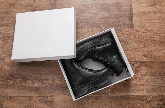 Foto nieuwe modieuze stijlvolle lederen vrouwelijke zwarte laarzen in doos op houten vloer bovenaanzicht