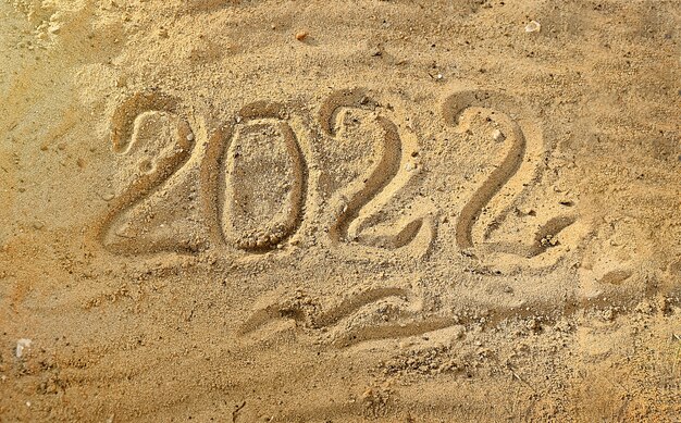 Nieuwjaar 2022 met de hand geschreven op nat zand op een strand aan zee Aftellen aan de vooravond van de vakantie