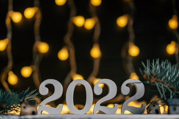 Nieuwjaar 2022. Witte houten nummers 2022 staan met kerstboomtakken tegen guirlande gloeilampen. Ruimte kopiëren